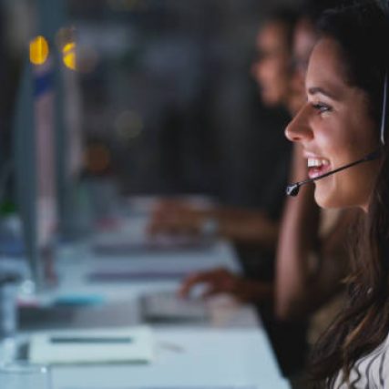 Cropped shot of an attractive young female call center agent working late in the office with her colleagues in the background
